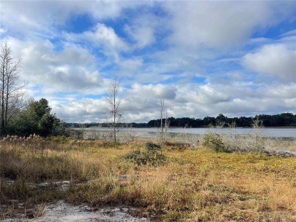 A grassy, undeveloped waterfront lot overlooks a large lake under a partly cloudy sky — GRAYS AIRPORT ROAD, LADY LAKE, FL