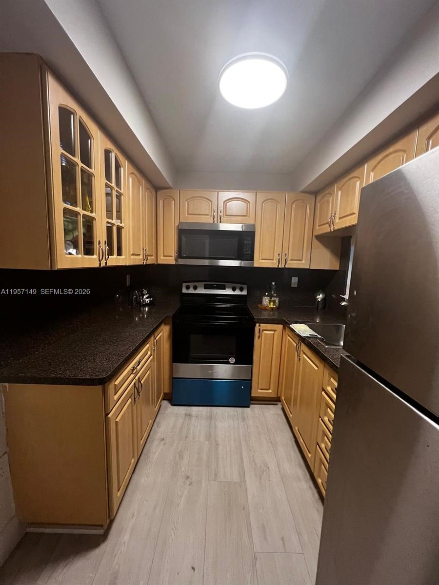 A galley kitchen features light wood cabinets, dark countertops, and stainless steel appliances — 11750 SW 18th St # 1, Miami FL 33175, MIAMI, FL