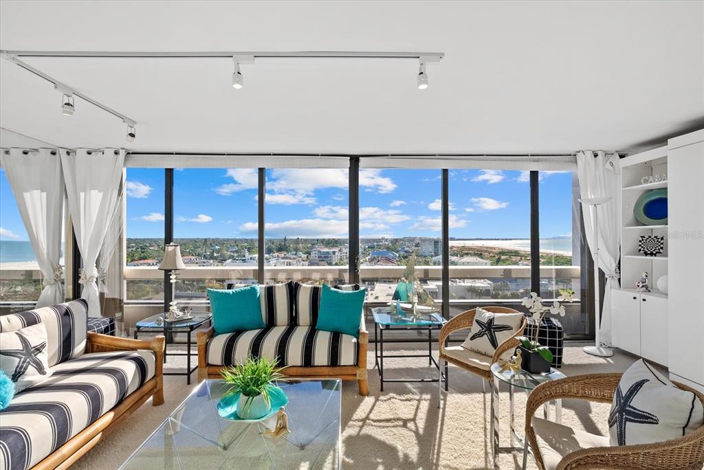A living room with striped furniture, glass tables, and floor-to-ceiling windows overlooking the ocean — 5400 OCEAN BOULEVARD UNIT 8-05, SARASOTA, FL