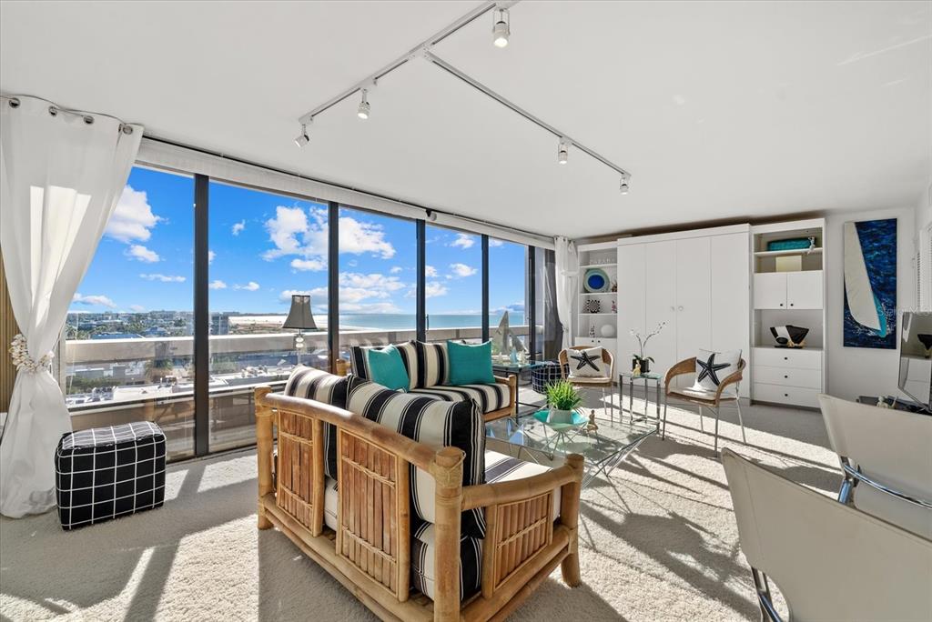 A living room with bamboo furniture, striped cushions, and floor-to-ceiling windows overlooking the ocean — 5400 OCEAN BOULEVARD UNIT 8-05, SARASOTA, FL
