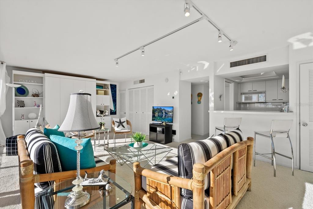 A living room with bamboo-framed striped sofas, a glass coffee table, and an open kitchen — 5400 OCEAN BOULEVARD UNIT 8-05, SARASOTA, FL