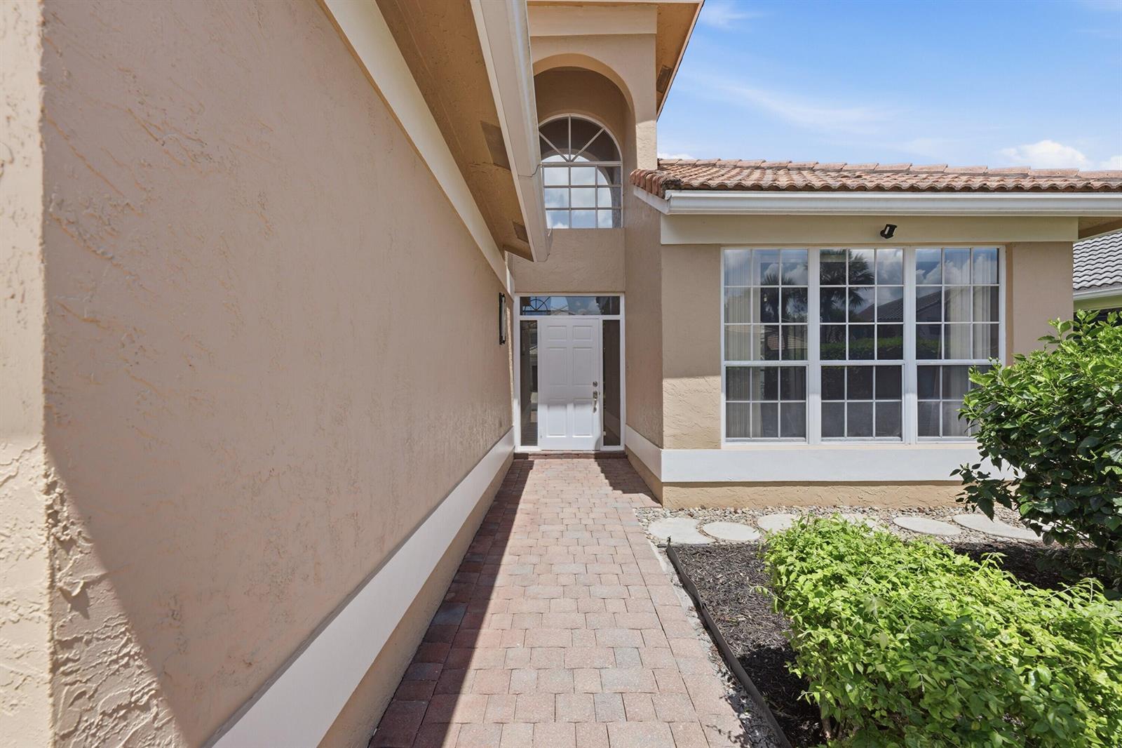 A paved walkway leads to the white front door of a tan stucco house — 18474 Old Princeton Lane, Boca Raton FL 33498, BOCA RATON, FL