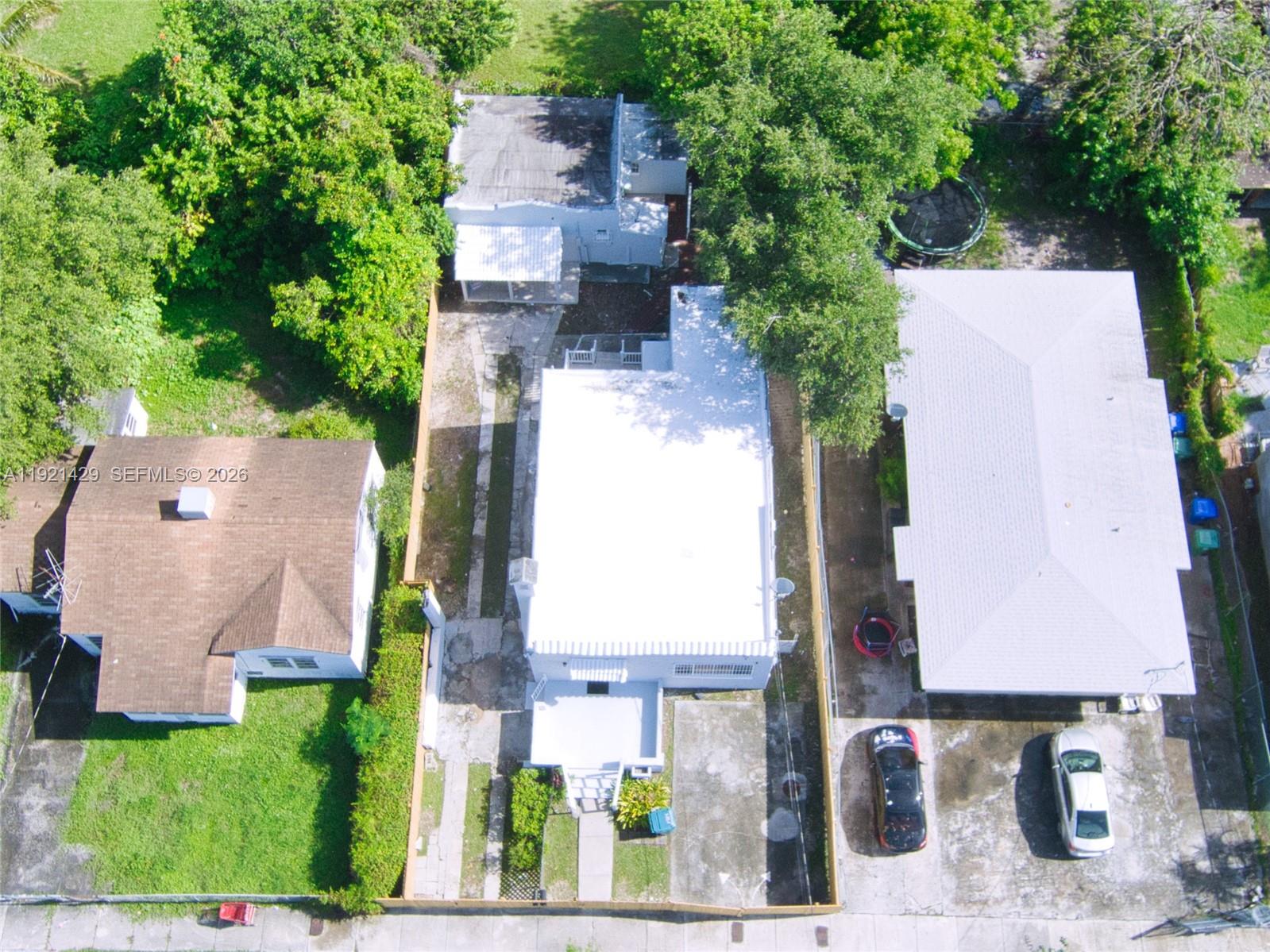 An aerial view shows three adjacent houses with white and brown roofs and paved driveways — 1845 NW 55th St, Miami FL 33142, MIAMI, FL
