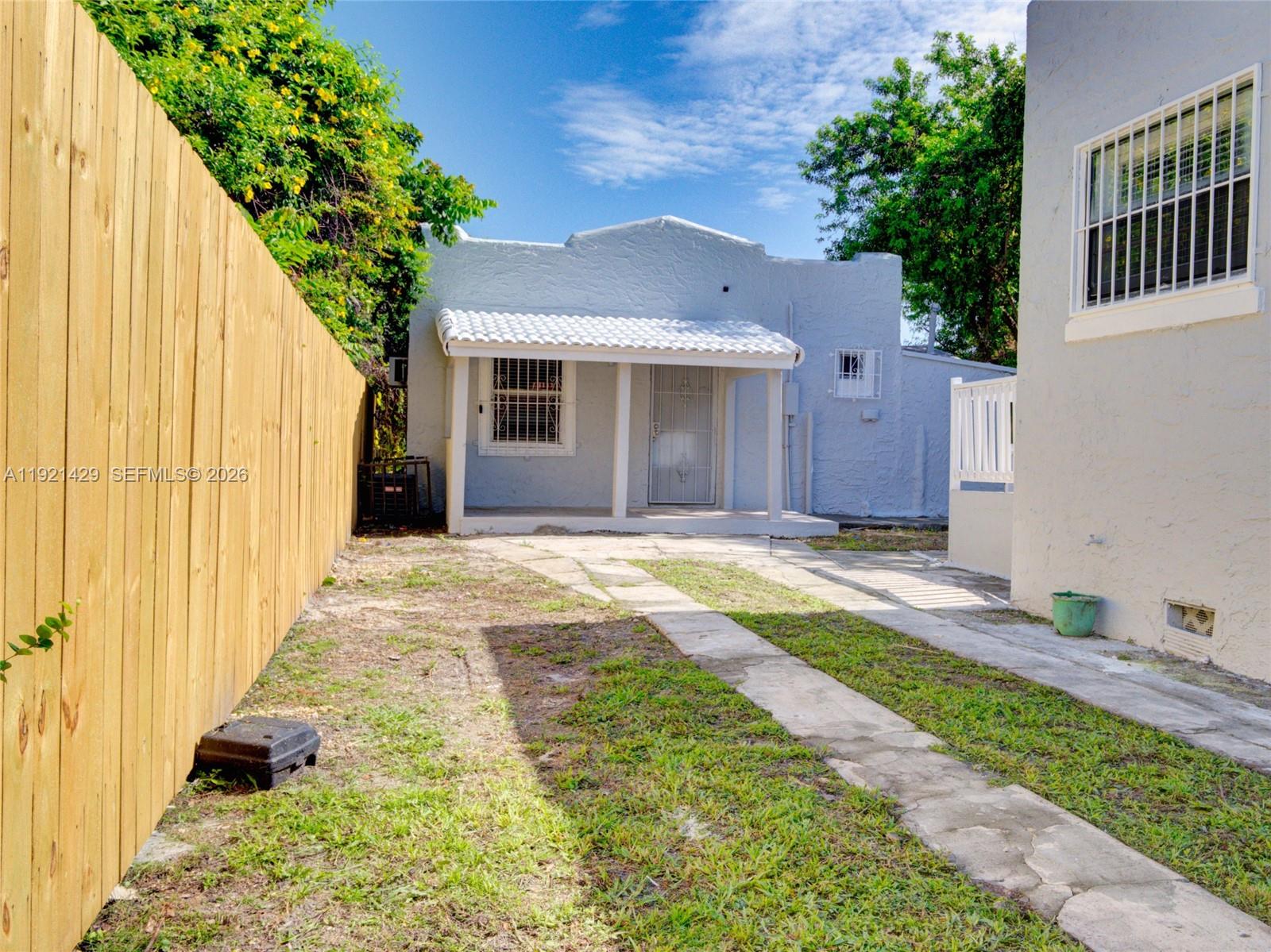 A small, light blue house with a covered porch sits behind a wooden fence — 1845 NW 55th St, Miami FL 33142, MIAMI, FL