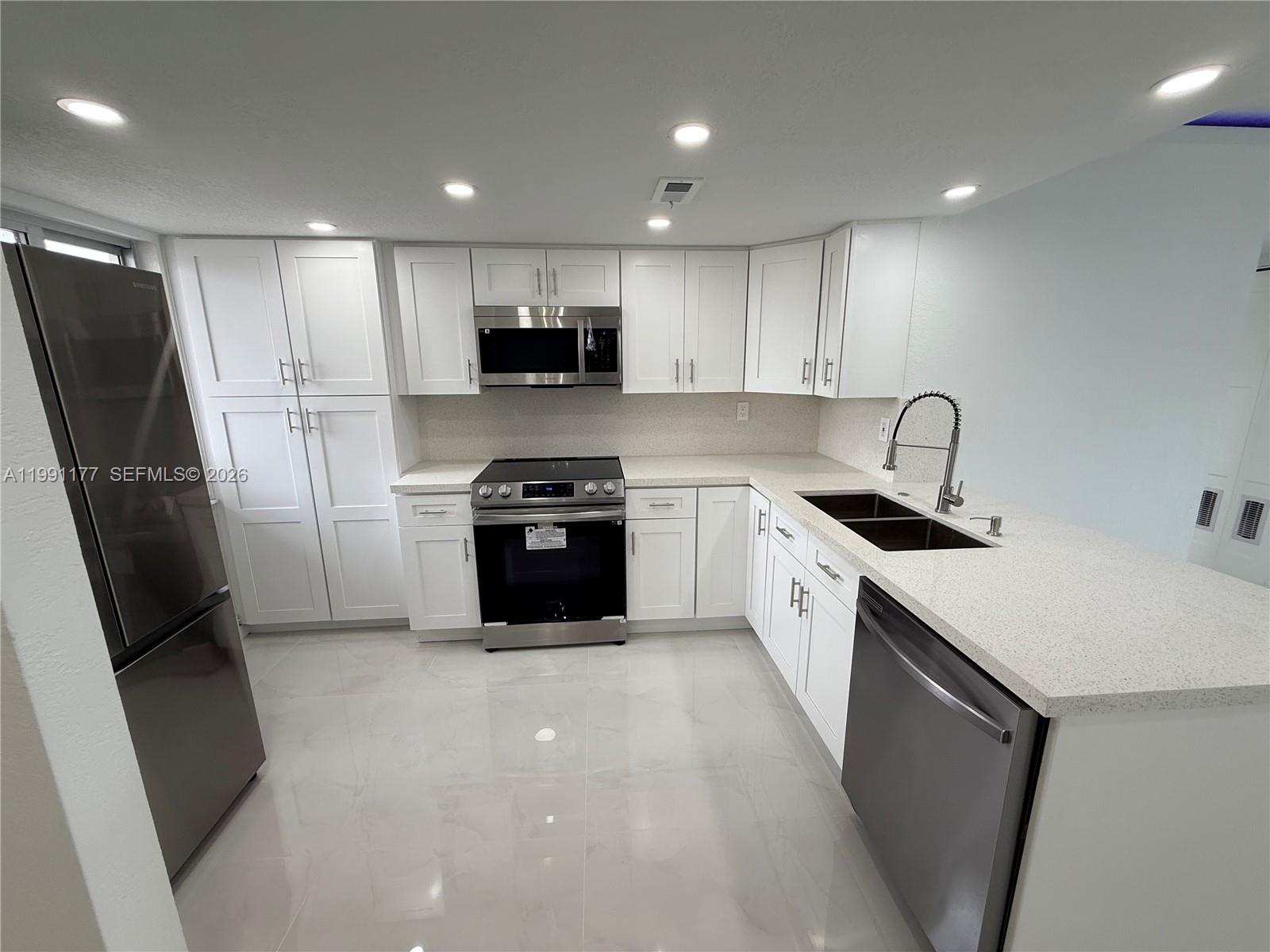A modern kitchen features white cabinetry, stainless steel appliances, and light-colored countertops — 9915 W Okeechobee Rd # 201, Hialeah Gardens FL 33016, HIALEAH GARDENS, FL