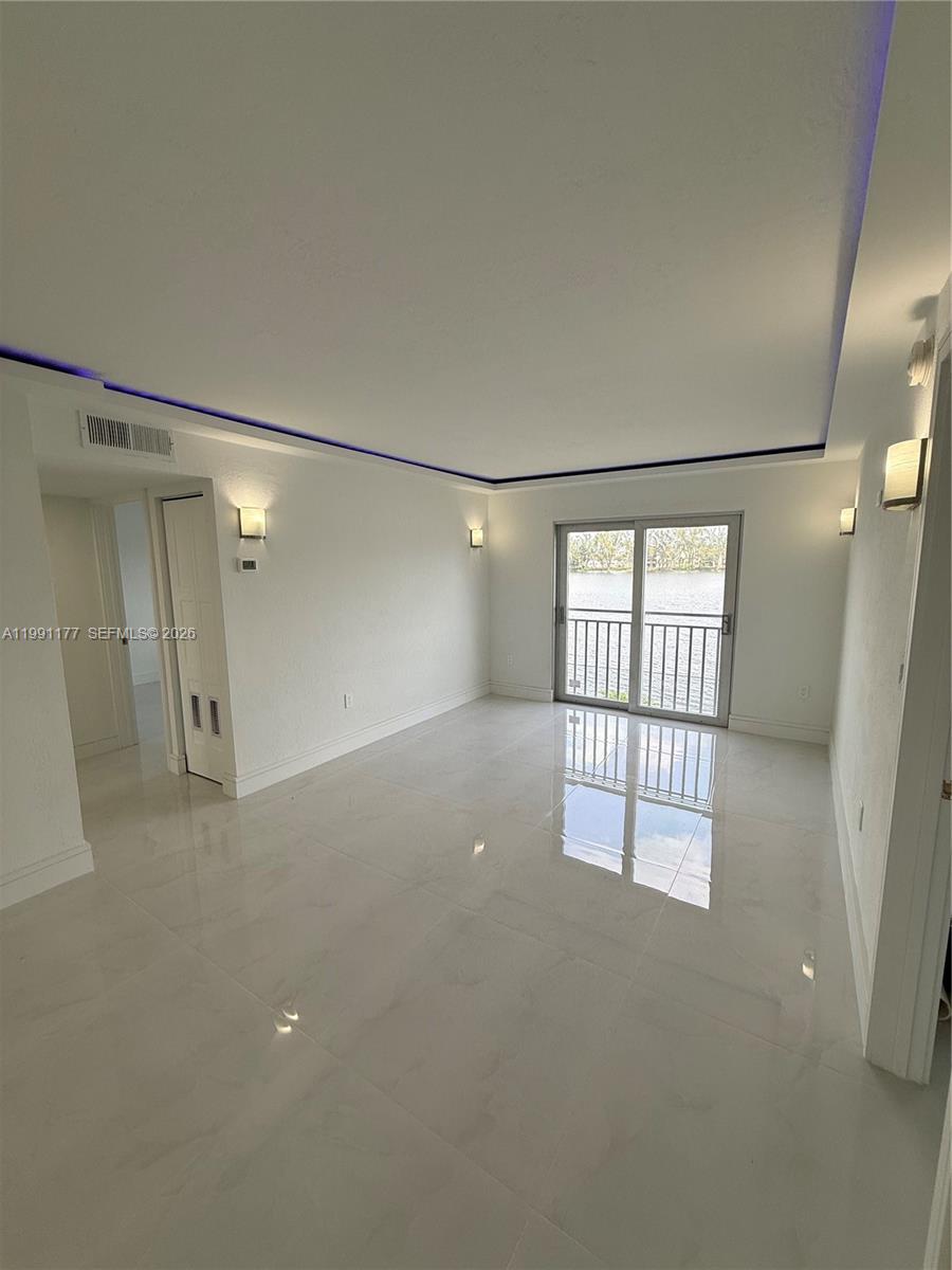 An empty room features white tile floors, recessed ceiling lighting, and a sliding glass door — 9915 W Okeechobee Rd # 201, Hialeah Gardens FL 33016, HIALEAH GARDENS, FL