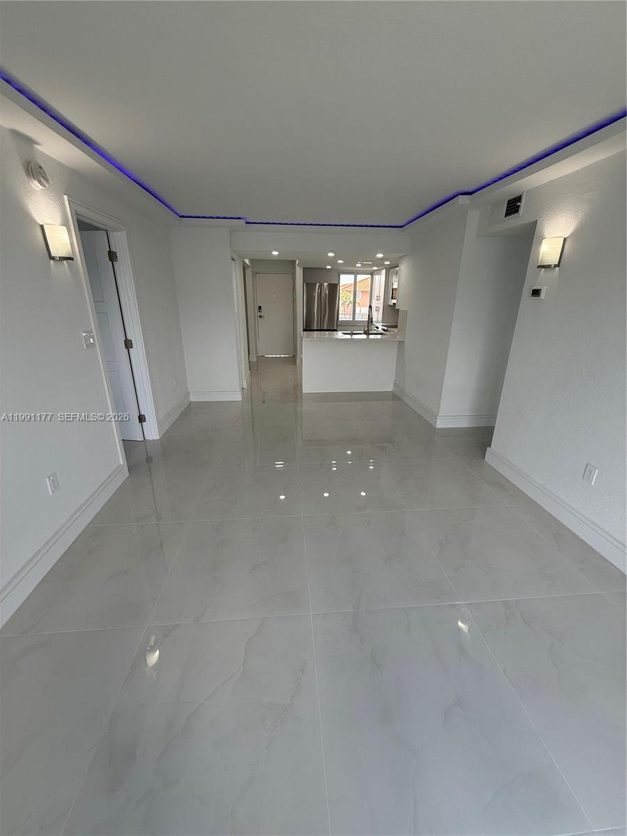 A bright, open-concept living area features white tile flooring, recessed lighting, and a kitchen beyond — 9915 W Okeechobee Rd # 201, Hialeah Gardens FL 33016, HIALEAH GARDENS, FL