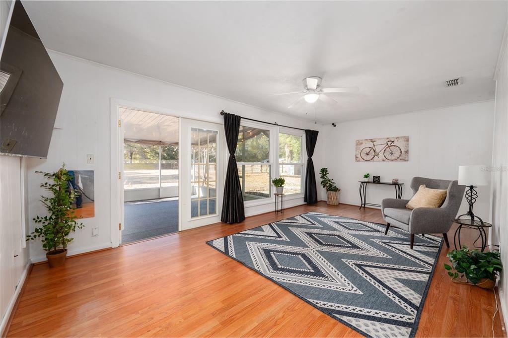 A living room features wood flooring, a geometric rug, a gray armchair, and sliding glass doors — 7220 SW 75TH STREET, GAINESVILLE, FL