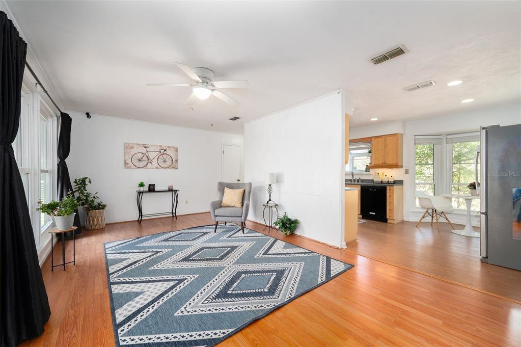 A living room with hardwood floors, a geometric rug, a gray armchair, and an adjacent kitchen — 7220 SW 75TH STREET, GAINESVILLE, FL