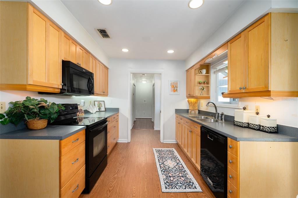 A galley kitchen features light wood cabinets, black appliances, gray countertops, and wood-look flooring — 7220 SW 75TH STREET, GAINESVILLE, FL