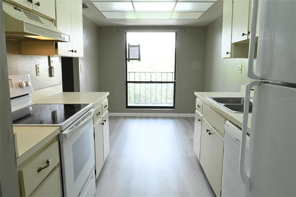 A galley-style kitchen features white appliances, light-colored cabinets, and a window overlooking a balcony — 2700 COVE CAY DRIVE UNIT 1-4G, CLEARWATER, FL