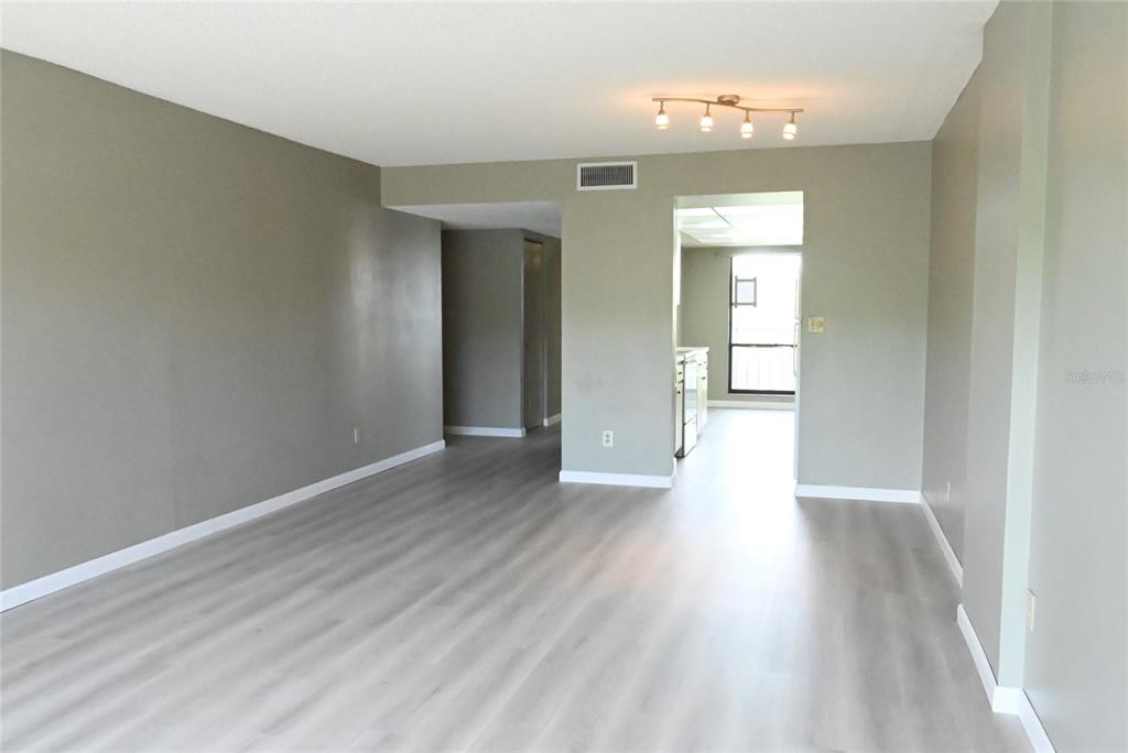 An empty living room with light gray wood-look flooring and neutral walls leads to a kitchen — 2700 COVE CAY DRIVE UNIT 1-4G, CLEARWATER, FL