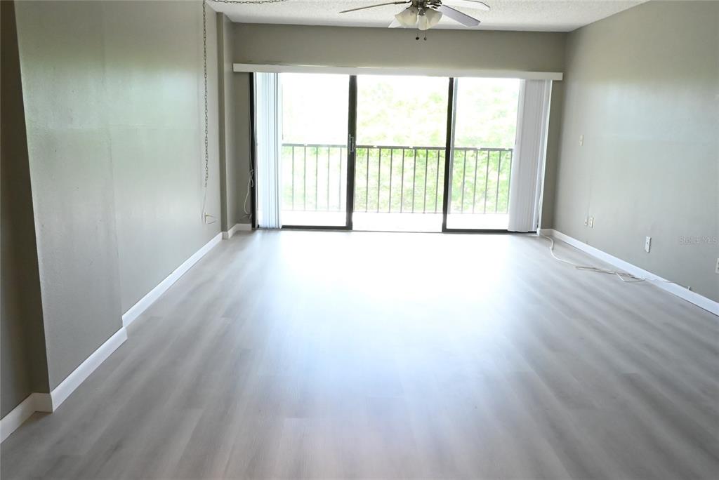 An empty living room features light-colored wood-look flooring, gray walls, and a sliding glass door — 2700 COVE CAY DRIVE UNIT 1-4G, CLEARWATER, FL