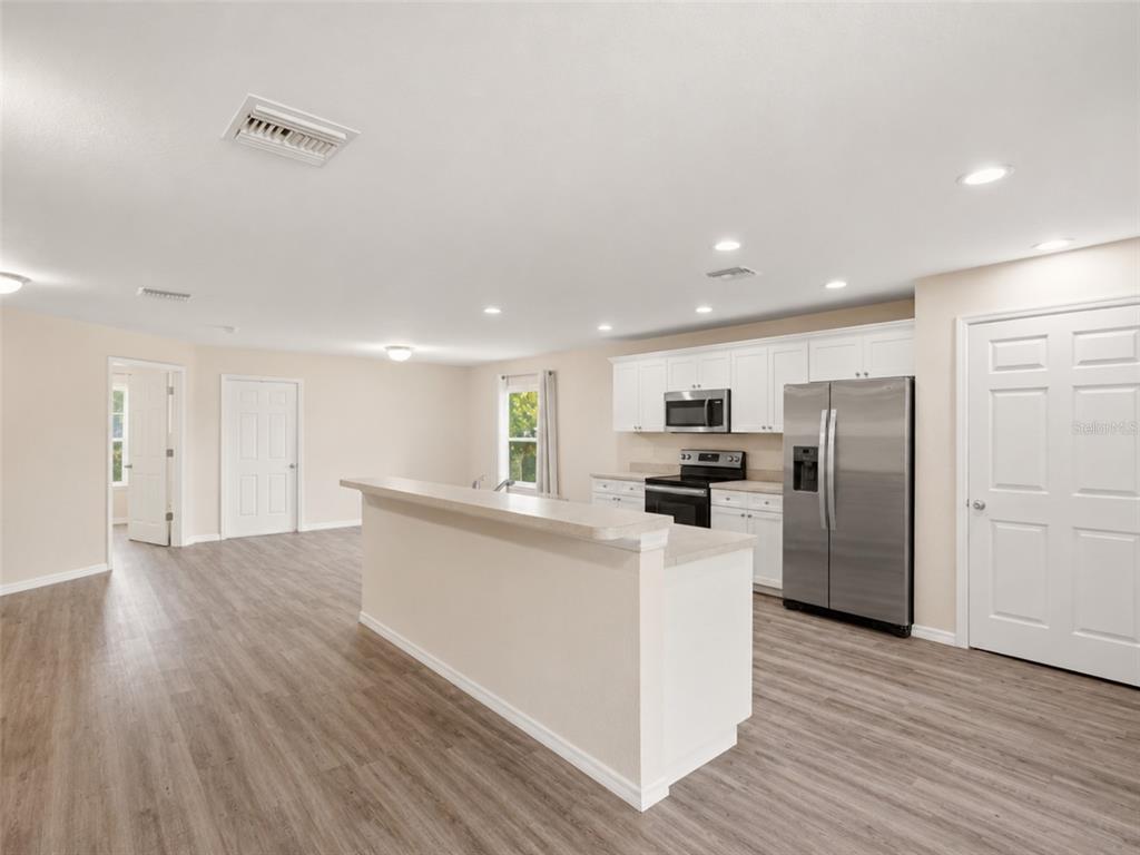 A kitchen with white cabinets, stainless steel appliances, and a breakfast bar on wood flooring — 1938 LILLIE STREET, FORT MYERS, FL