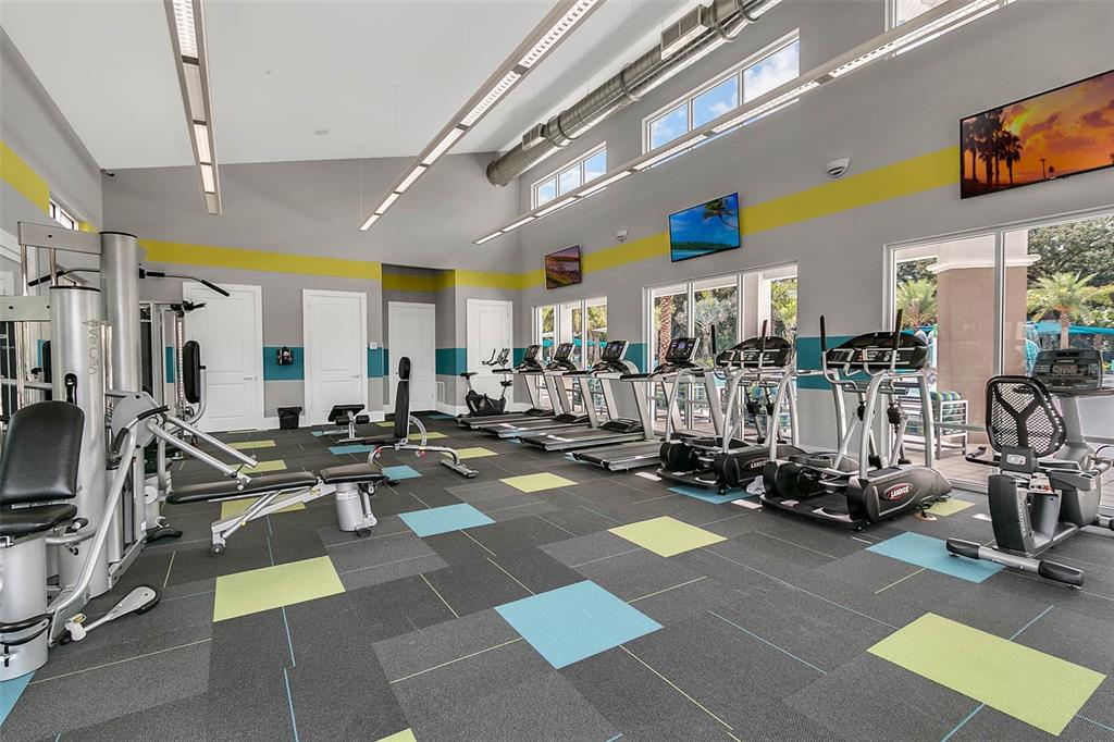 A gym features various exercise machines, gray carpet tiles with colorful accents, and large windows — 2618 SANTOSH COVE, KISSIMMEE, FL