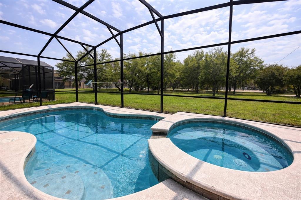 A screened-in swimming pool and attached hot tub overlook a grassy backyard with trees — 2618 SANTOSH COVE, KISSIMMEE, FL