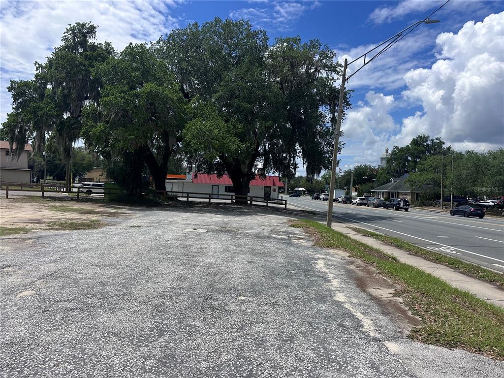 A gravel lot sits beside a road with large oak trees and a small building — US hwy 41 E GRACE STREET STREET E, INVERNESS, FL