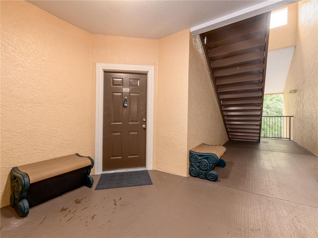 An exterior apartment entryway features a brown door, two benches, and an adjacent staircase — 5125 PALM SPRINGS BOULEVARD UNIT 2206, TAMPA, FL