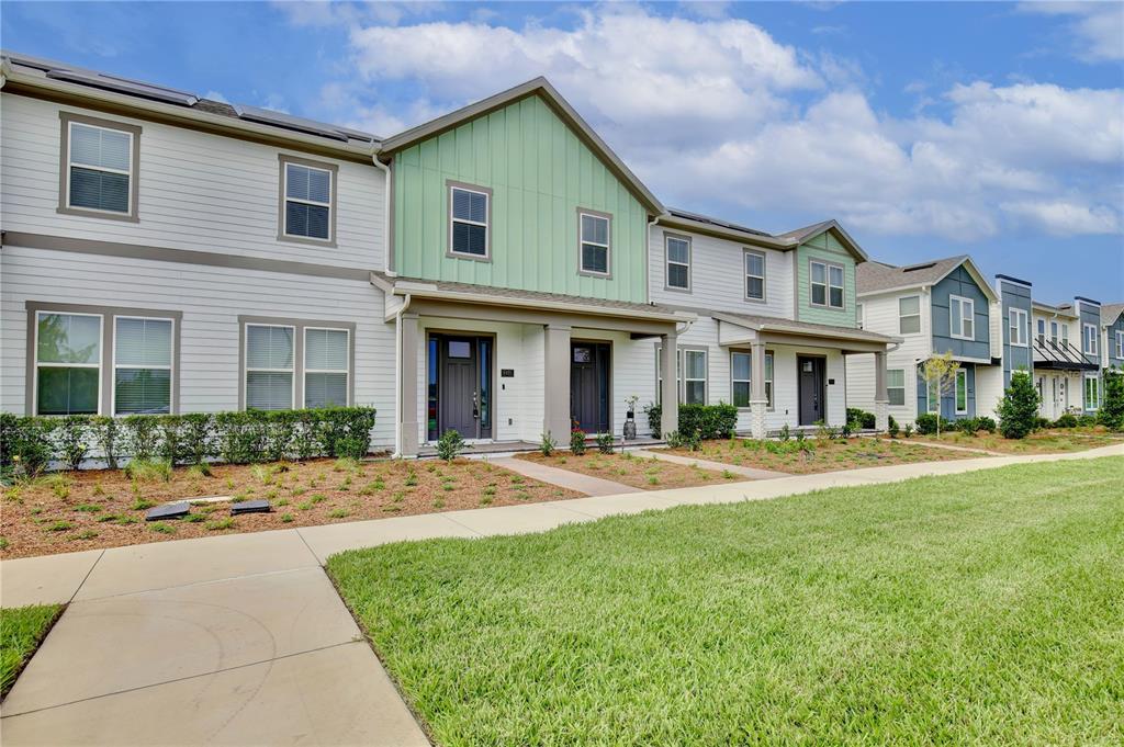 A row of modern two-story townhouses features white siding, green accents, and front porches — 6491 CYRILS DRIVE, ST CLOUD, FL