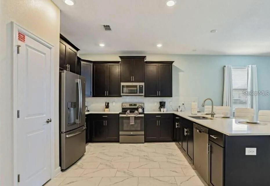 A kitchen with dark cabinets, stainless steel appliances, white countertops, and light-colored tile flooring — 1575 PLUNKER DRIVE, DAVENPORT, FL