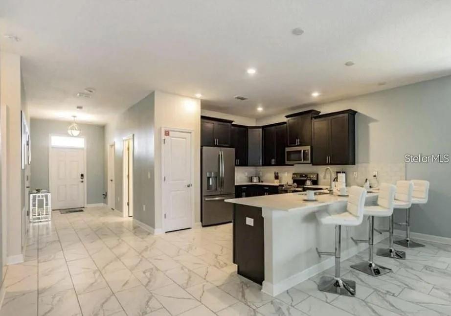 A kitchen with dark cabinets, stainless steel appliances, and a white island with bar stools — 1575 PLUNKER DRIVE, DAVENPORT, FL