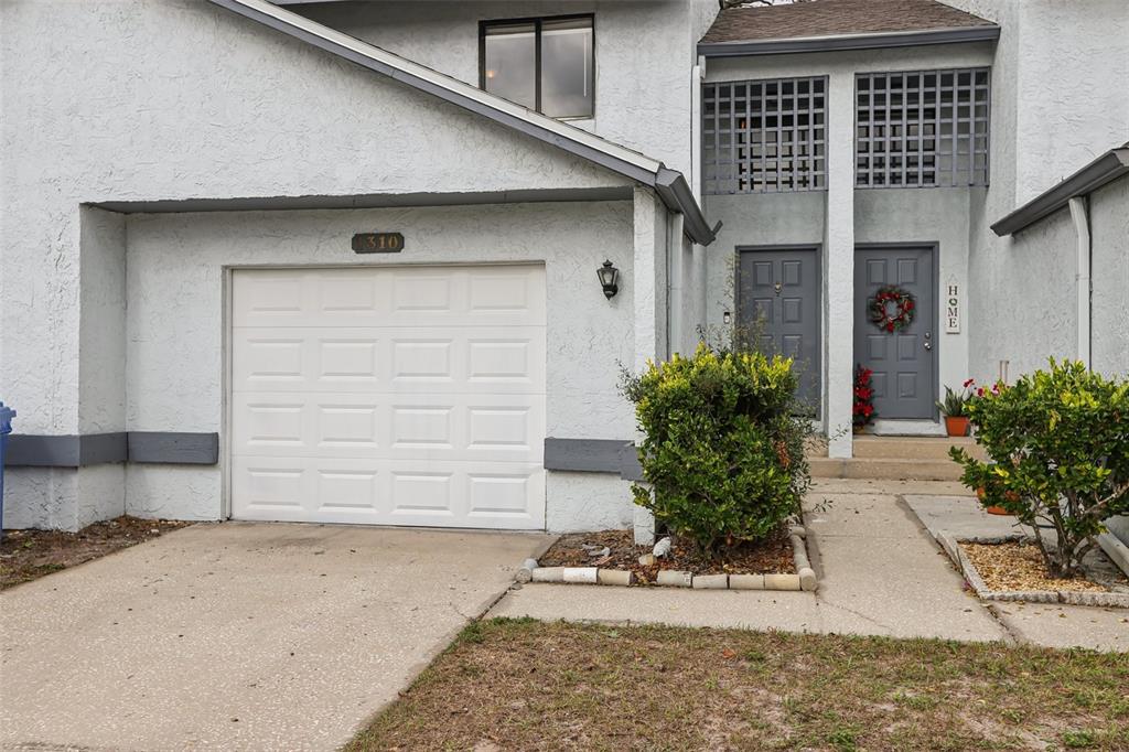 A two-story townhouse exterior features a white garage, gray doors, and a small front garden — 1310 MOUNTAIN VIEW DRIVE UNIT 105, TAMPA, FL