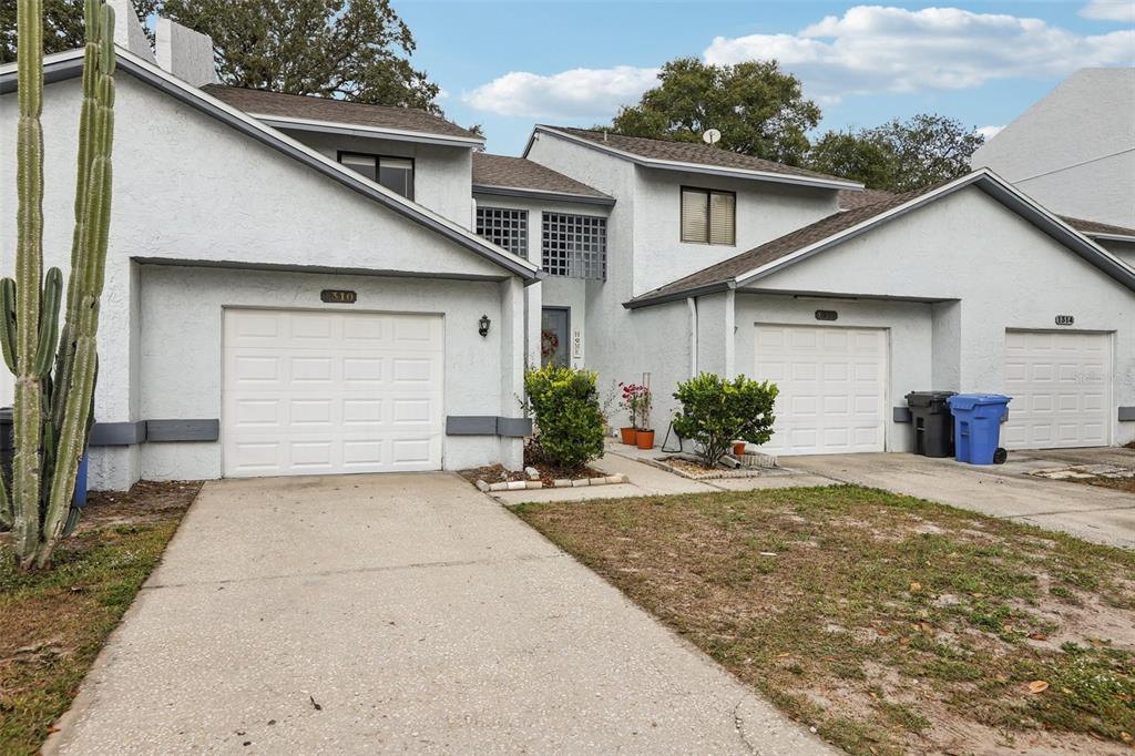 A multi-unit residential building with white stucco siding, three garage doors, and a tall cactus — 1310 MOUNTAIN VIEW DRIVE UNIT 105, TAMPA, FL