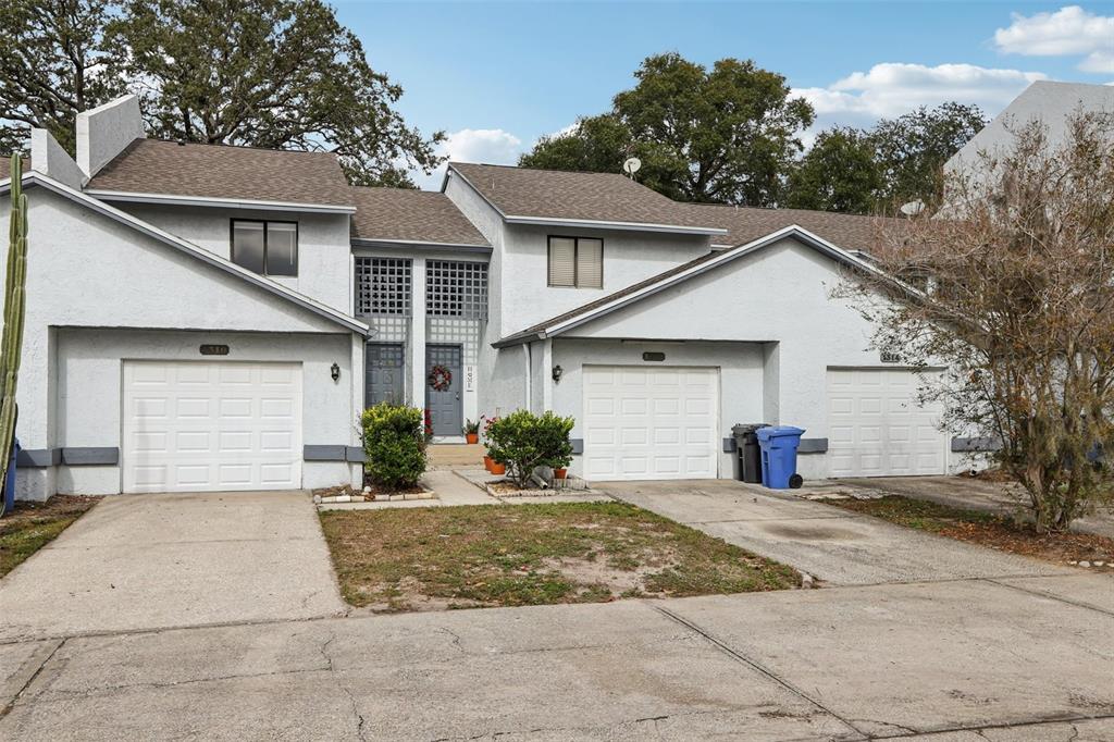 A row of three attached townhomes with white stucco siding, gray roofs, and concrete driveways — 1310 MOUNTAIN VIEW DRIVE UNIT 105, TAMPA, FL