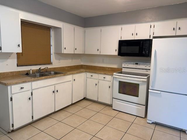 A kitchen features white cabinets, tan laminate countertops, white appliances, and light-colored tile flooring — 2802 7TH STREET, ST CLOUD, FL