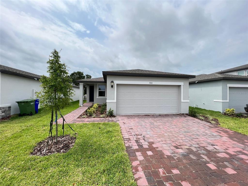 A single-story house with a gray exterior, a two-car garage, and a brick paver driveway — 1848 CARNOSTIE ROAD, WINTER HAVEN, FL