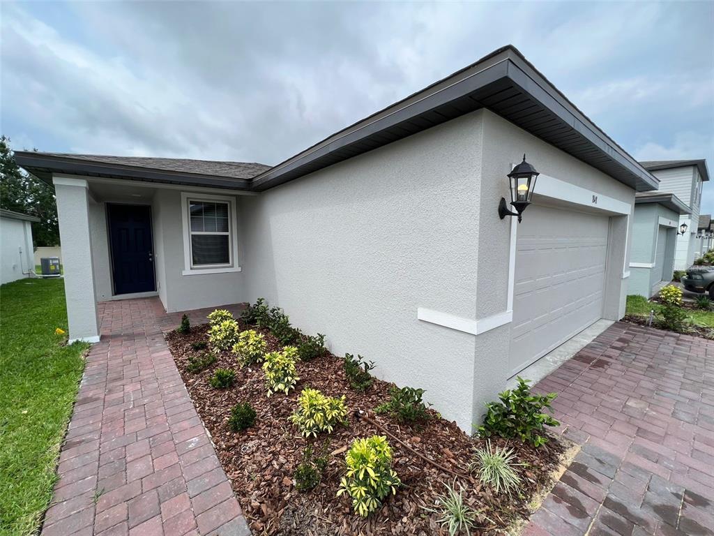 A single-story house exterior features a gray stucco facade, a brick walkway, and a garage — 1848 CARNOSTIE ROAD, WINTER HAVEN, FL