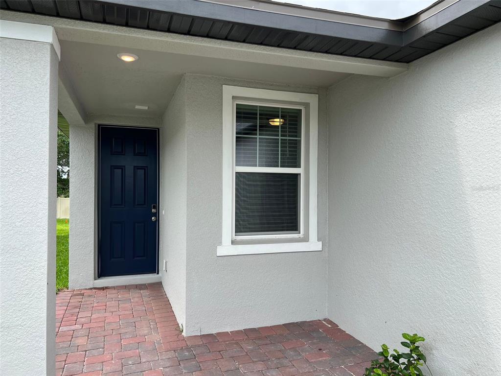 A dark blue front door and a single window are set into a gray stucco wall — 1848 CARNOSTIE ROAD, WINTER HAVEN, FL