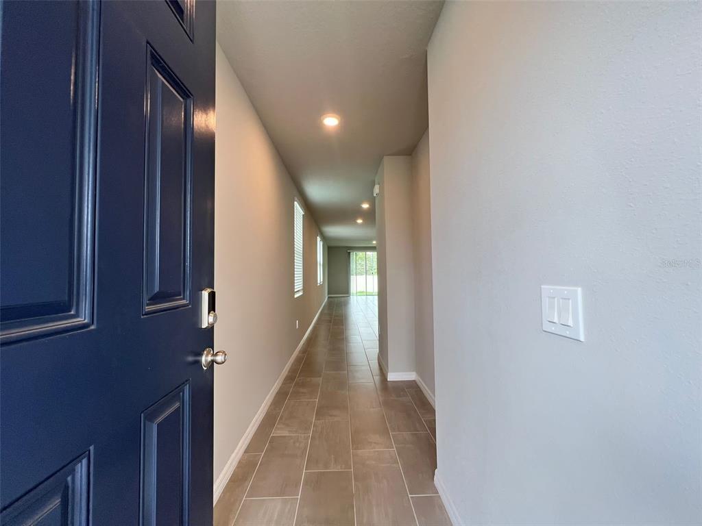 A long hallway with tile flooring leads from a dark blue front door toward a window — 1848 CARNOSTIE ROAD, WINTER HAVEN, FL