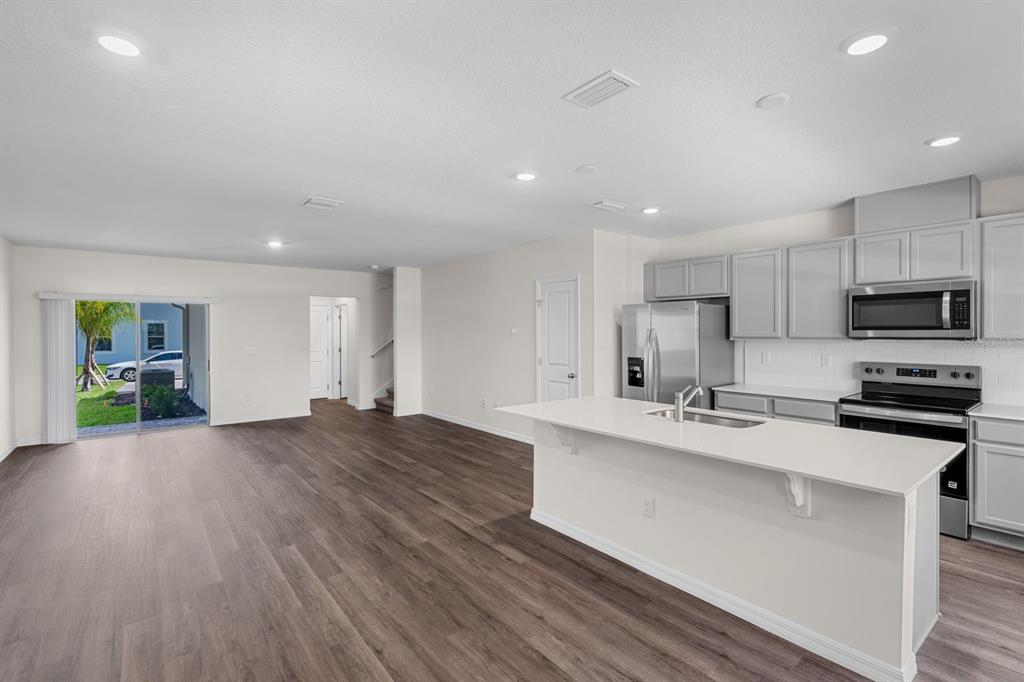 An open-concept kitchen and living area featuring light gray cabinets, white countertops, and wood-look flooring — 16509 BARBOURS CREEK WAY, WINTER GARDEN, FL