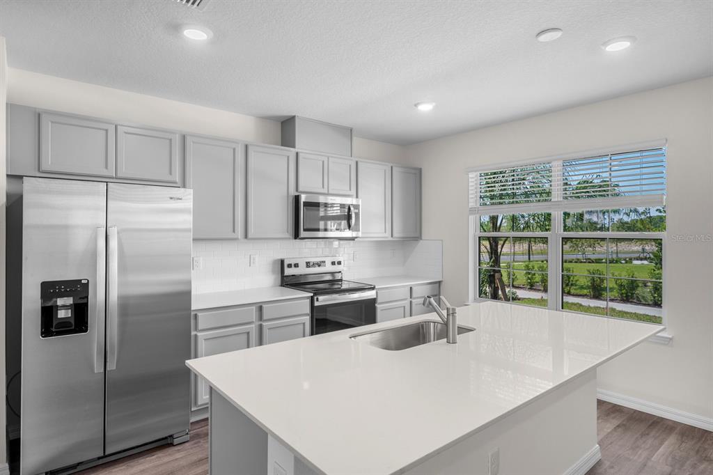 A modern kitchen features gray cabinets, stainless steel appliances, a white island, and large windows — 16509 BARBOURS CREEK WAY, WINTER GARDEN, FL