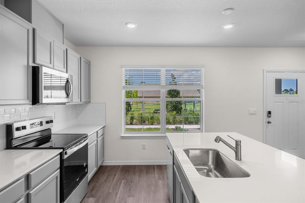 A modern kitchen features gray cabinets, white countertops, a center island, and a large window — 16509 BARBOURS CREEK WAY, WINTER GARDEN, FL