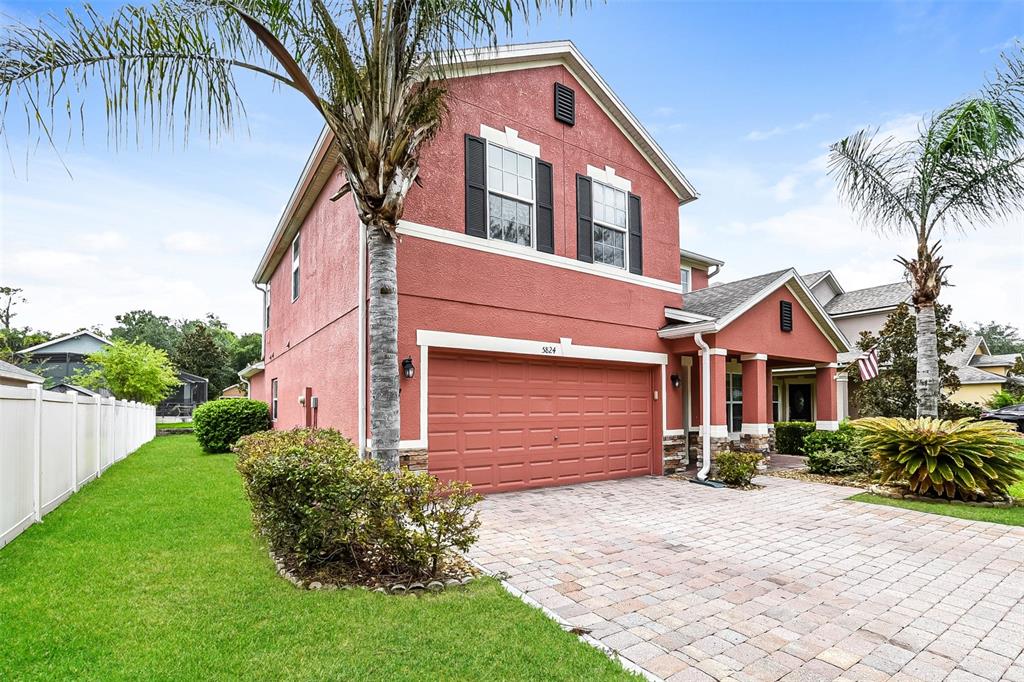 A two-story red stucco house features a two-car garage, palm trees, and a paved driveway — 5824 GREAT EGRET DRIVE, SANFORD, FL
