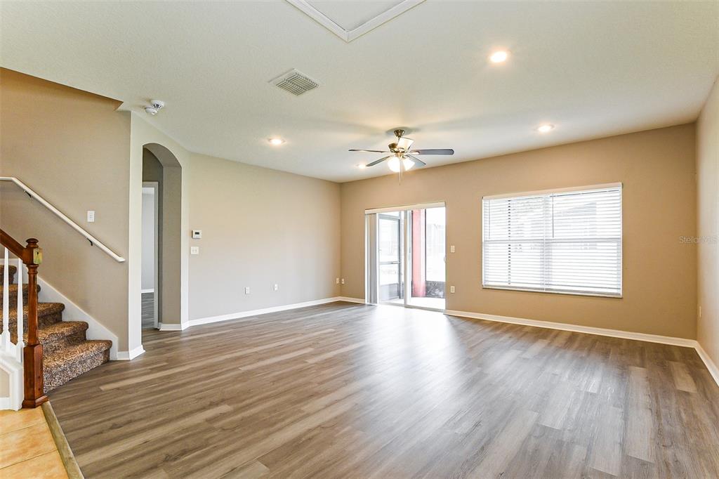 An empty living room features wood-look flooring, a ceiling fan, and a staircase — 5824 GREAT EGRET DRIVE, SANFORD, FL