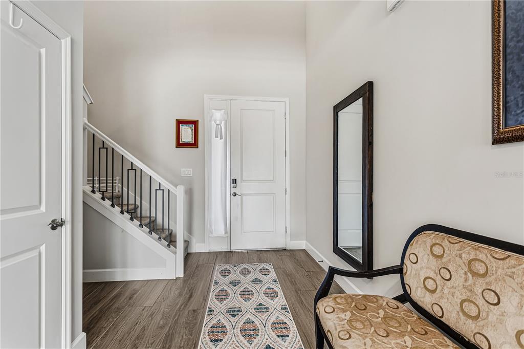 An entryway features wood-look flooring, a staircase with black railings, a front door, and a mirror — 264 LADY ALICE DRIVE, DAVENPORT, FL