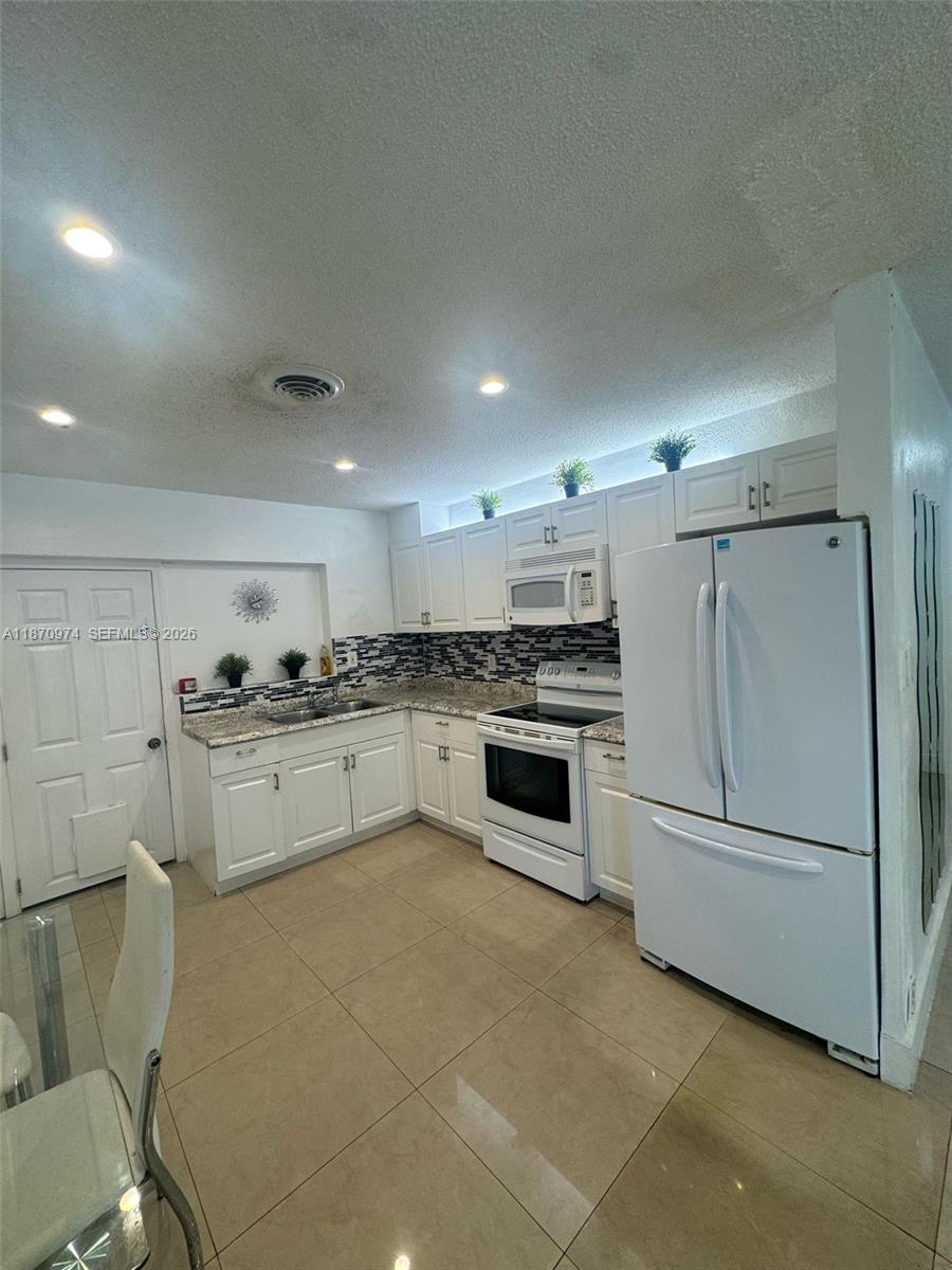 A kitchen features white cabinets, stainless steel appliances, granite countertops, and a tiled floor — 4808 NW 27th Ter, Tamarac FL 33309, TAMARAC, FL