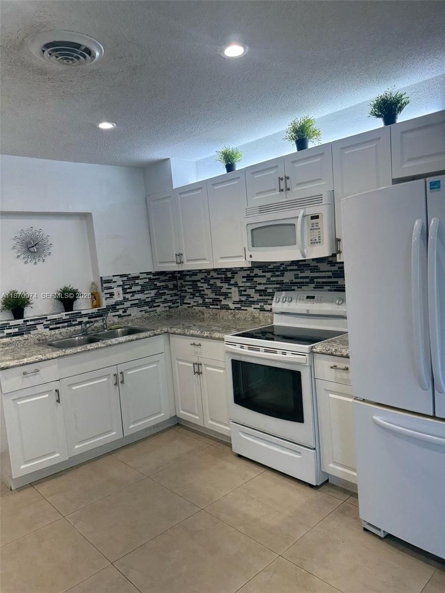 A kitchen features white cabinets, a white stove, a microwave, and a tiled backsplash — 4808 NW 27th Ter, Tamarac FL 33309, TAMARAC, FL