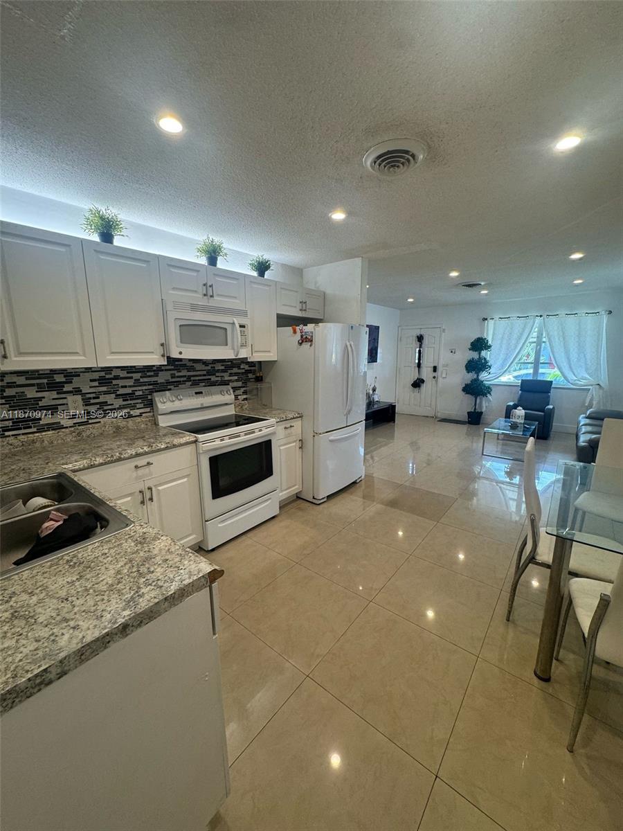 A kitchen with white cabinets and granite countertops opens into a tiled living area — 4808 NW 27th Ter, Tamarac FL 33309, TAMARAC, FL