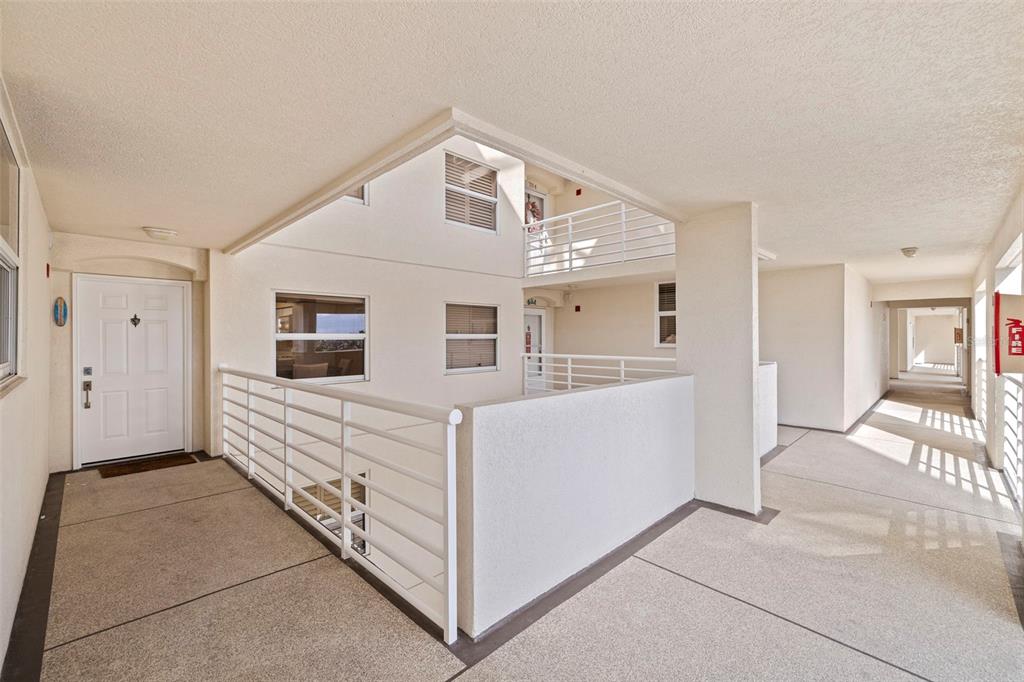 An outdoor apartment building walkway features a white door, metal railings, and concrete flooring — 6105 BAHIA DEL MAR CIRCLE UNIT 683, ST PETERSBURG, FL