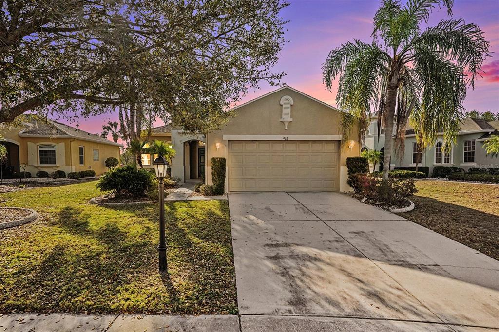 A single-story suburban house with a two-car garage, a concrete driveway, and a palm tree — 918 REGAL MANOR WAY, SUN CITY CENTER, FL
