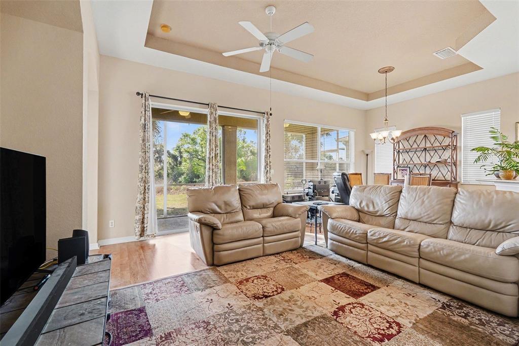 A living room with a tray ceiling, beige leather sofas, and a view of the backyard — 918 REGAL MANOR WAY, SUN CITY CENTER, FL