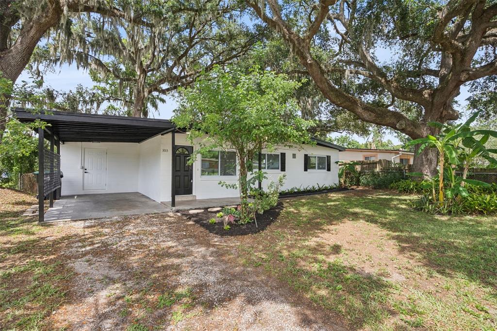 A white single-story house with a black carport and a large oak tree in front — 3013 KELVINGTON DRIVE, ORLANDO, FL