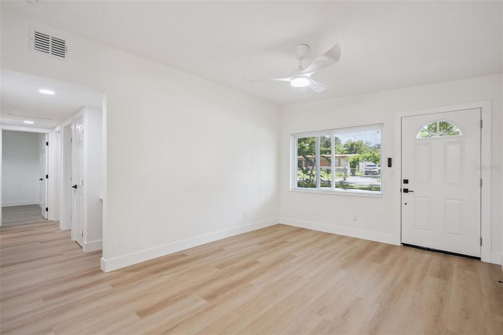 A bright, empty living room features light wood-look flooring, white walls, a ceiling fan, and a window — 3013 KELVINGTON DRIVE, ORLANDO, FL