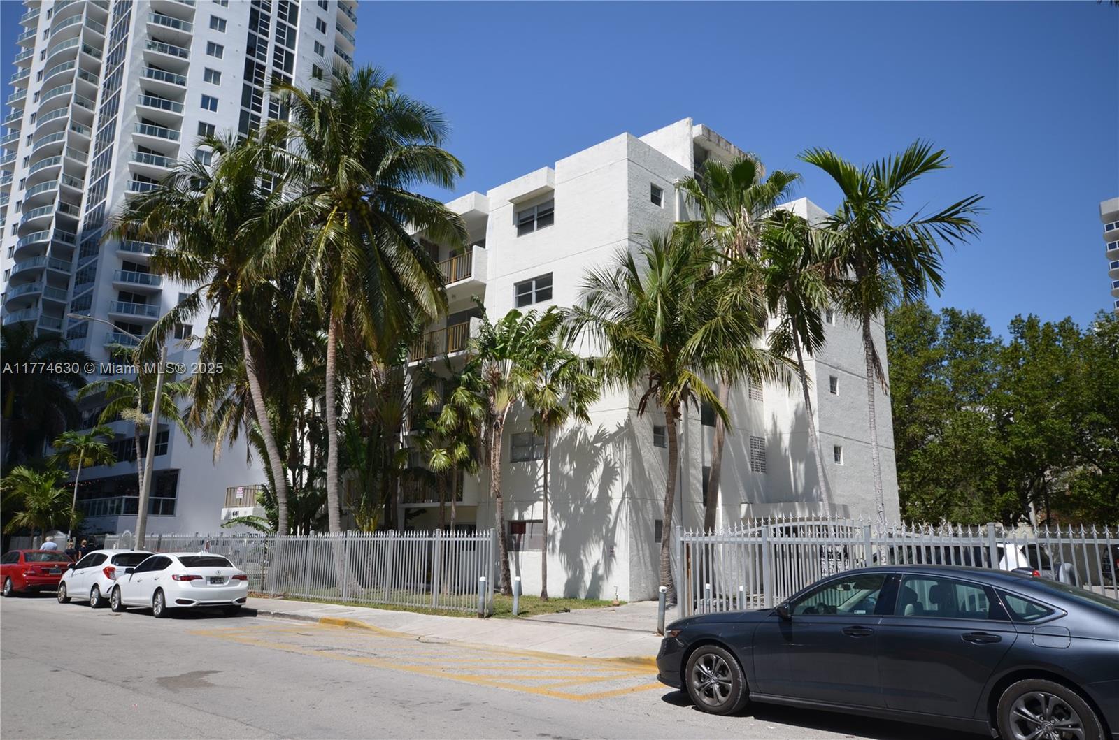 A multi-story white apartment building stands behind a metal fence with palm trees in front — 601 NE 22nd St, Miami FL 33137, MIAMI, FL
