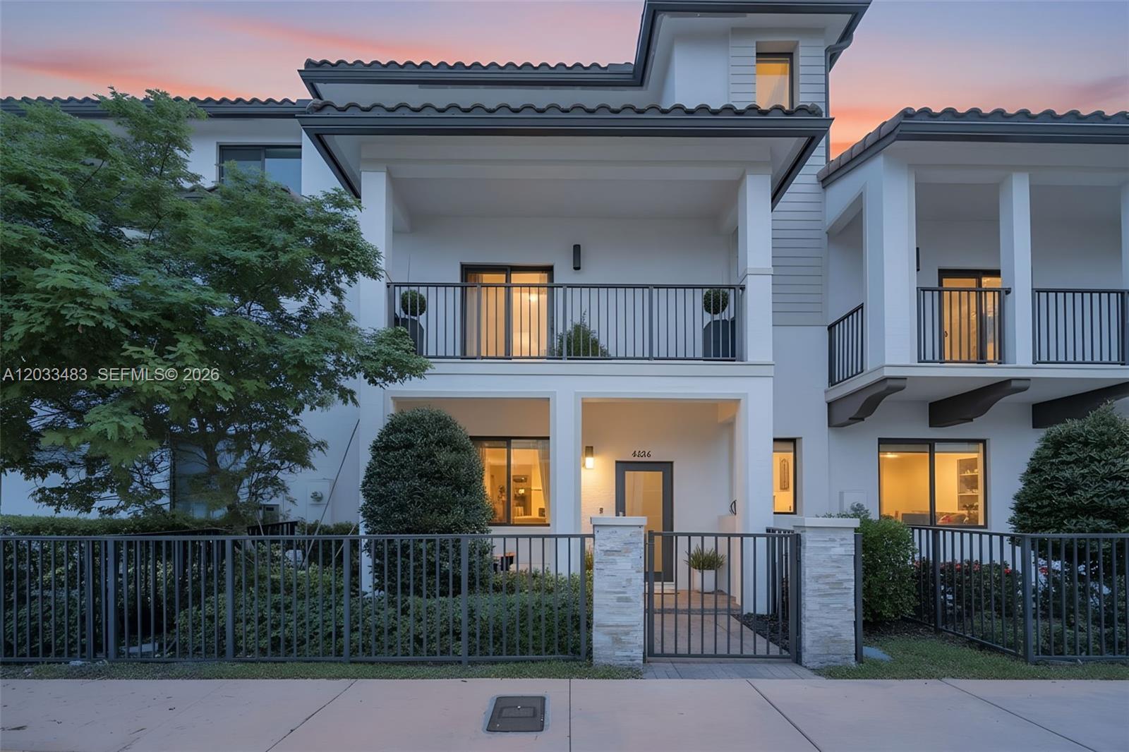 A two-story townhouse features a gated front courtyard, a second-floor balcony, and white stucco walls — 4256 NW 83rd Ave, Doral FL 33166, DORAL, FL