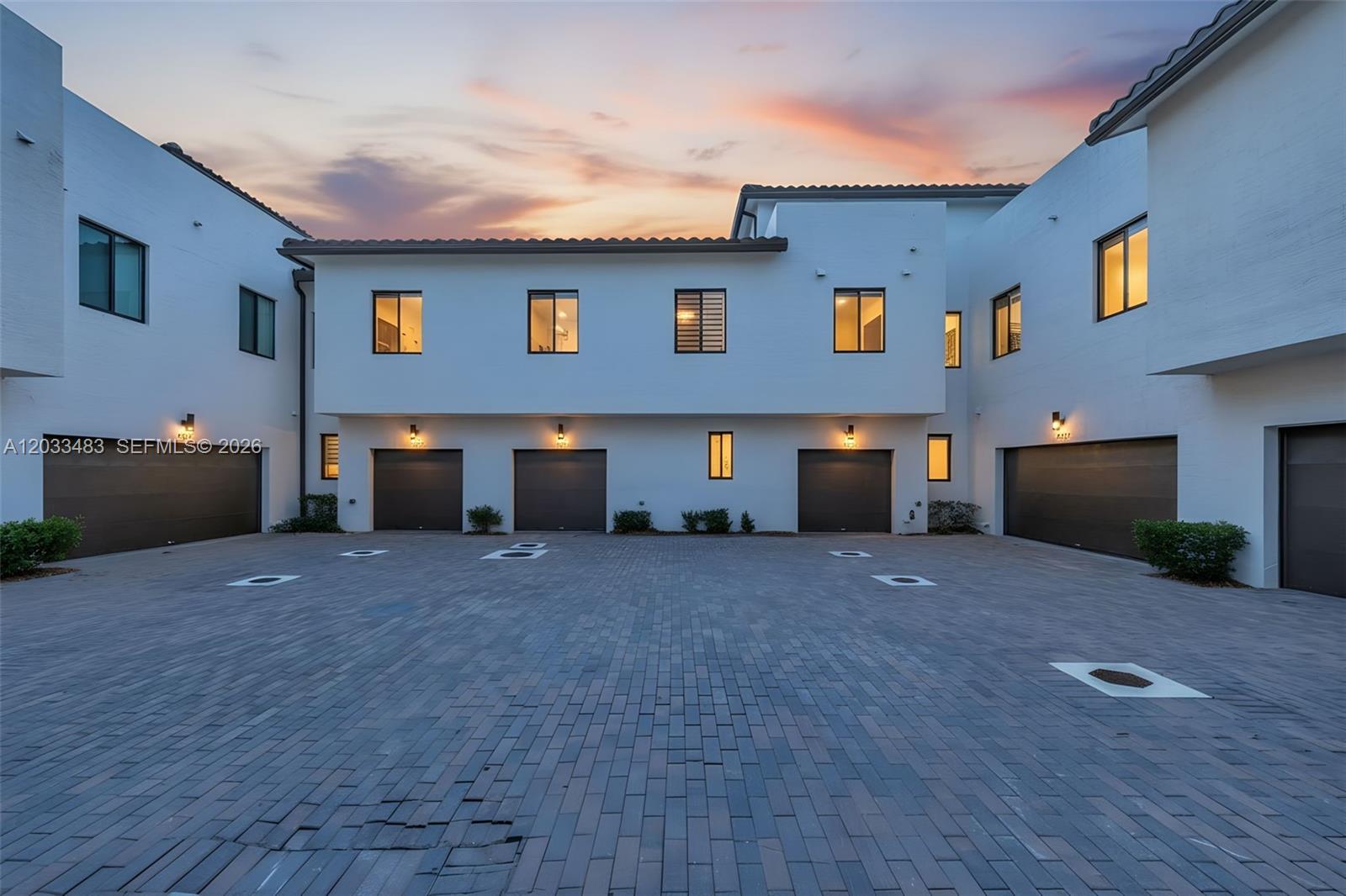 A courtyard with brick pavers leads to several garage doors of a modern white townhouse complex — 4256 NW 83rd Ave, Doral FL 33166, DORAL, FL